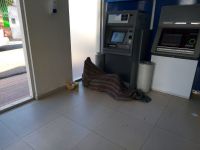 Un joven en situación de calle duerme en los cajeros automáticos bancarios